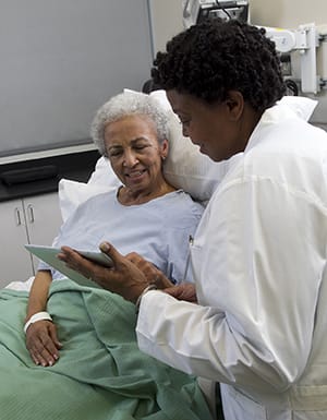 Doctor with electronic tablet talking to woman in hospital bed.