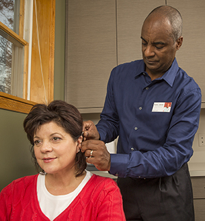 Health care provider fitting woman with hearing aid.