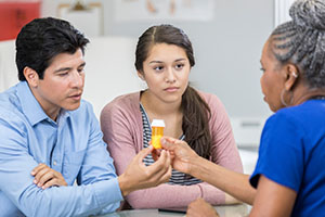 Father and daughter speaking with pharmacist about medications.