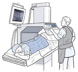 Patient lying face down on table under scanner with health care provider looking at monitor.